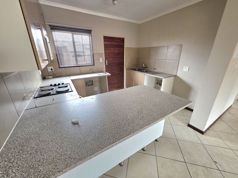 A functional kitchen featuring built-in cabinetry, laminate countertops, an electric hob, and a double sink, finished with neutral wall paint and ceramic floor tiles.