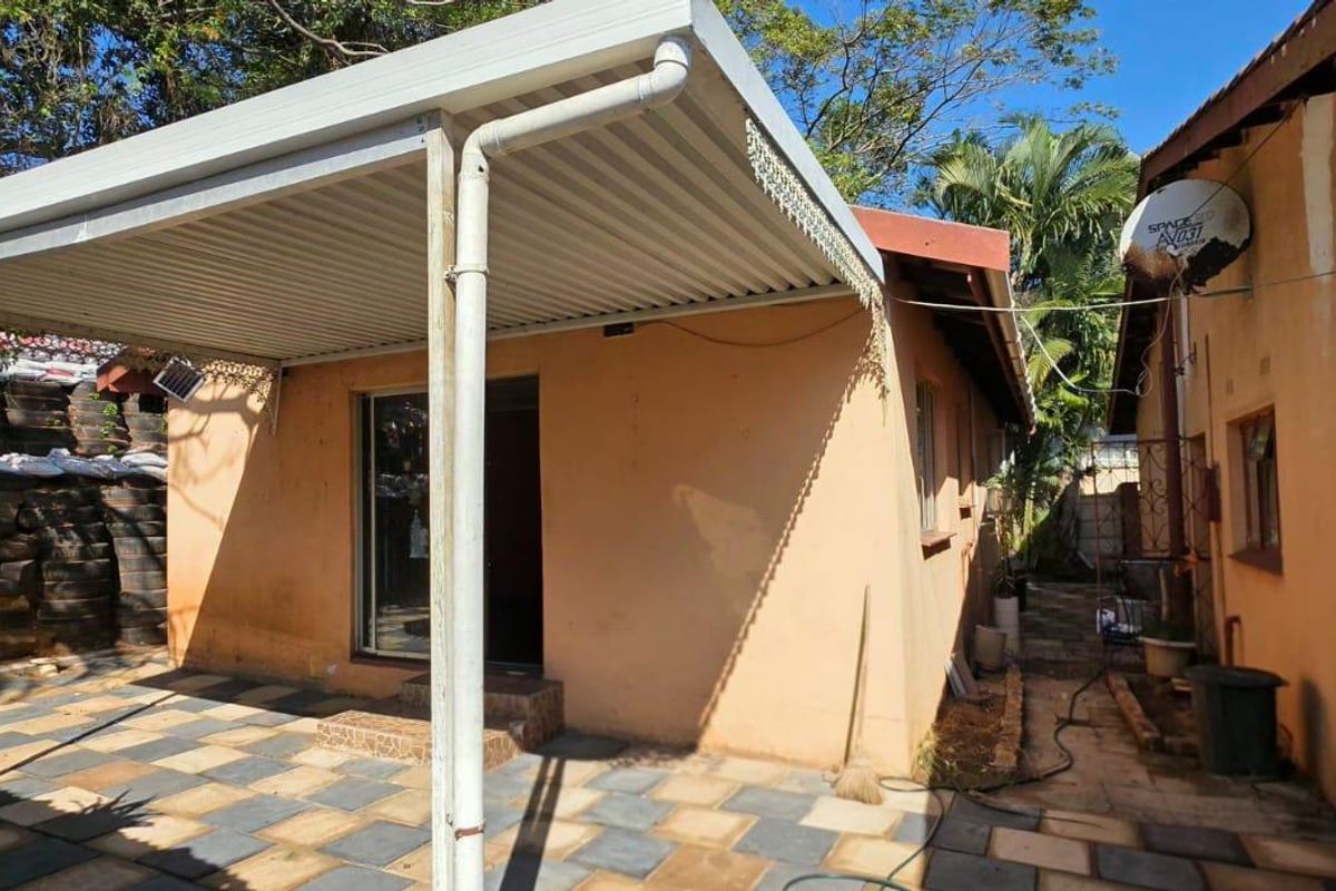 Rear exterior view showing a covered patio area with tiled flooring and weathered exterior wall finishes.