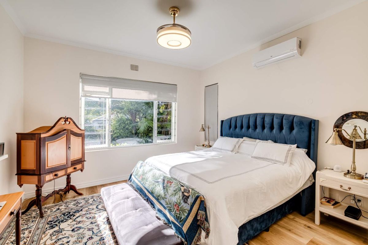 A well-maintained bedroom featuring timber flooring, a split-system air conditioning unit, and a large window providing natural light.