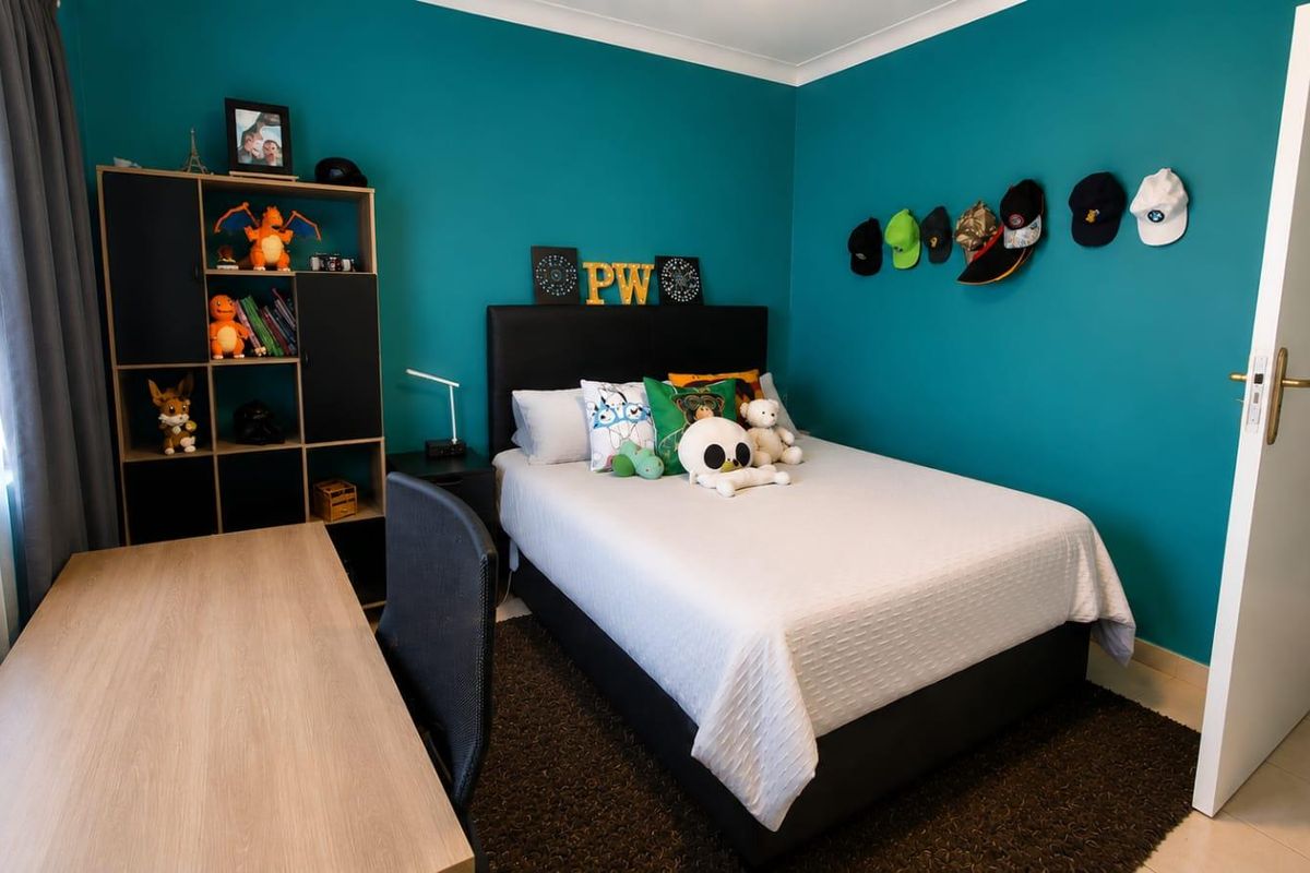 A well-maintained bedroom featuring bold teal accent walls, tiled flooring, and neutral window treatments.