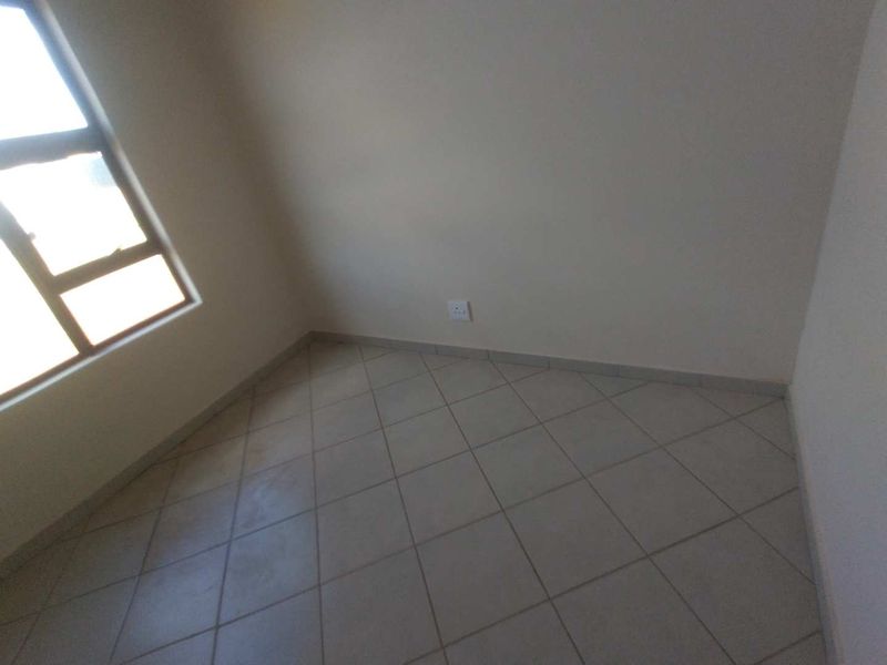 A vacant bedroom featuring neutral tiled flooring and a large window, providing a clean, blank canvas for interior design.