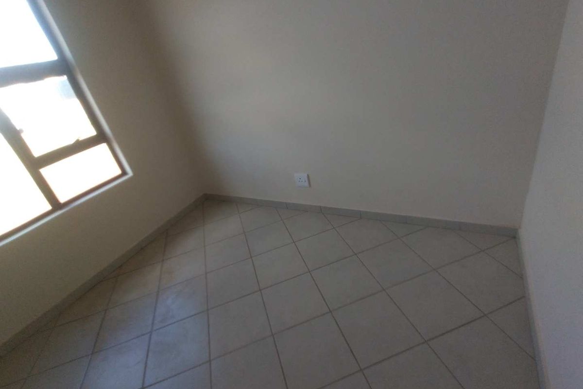 A vacant bedroom featuring neutral tiled flooring and a large window, providing a clean, blank canvas for interior design.