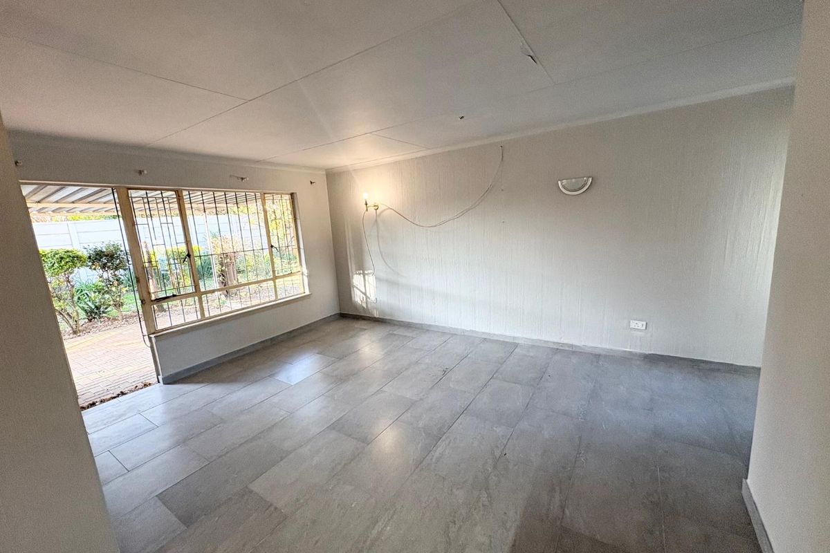 An empty living room featuring large windows with security bars, tiled flooring, and direct access to an outdoor patio area.