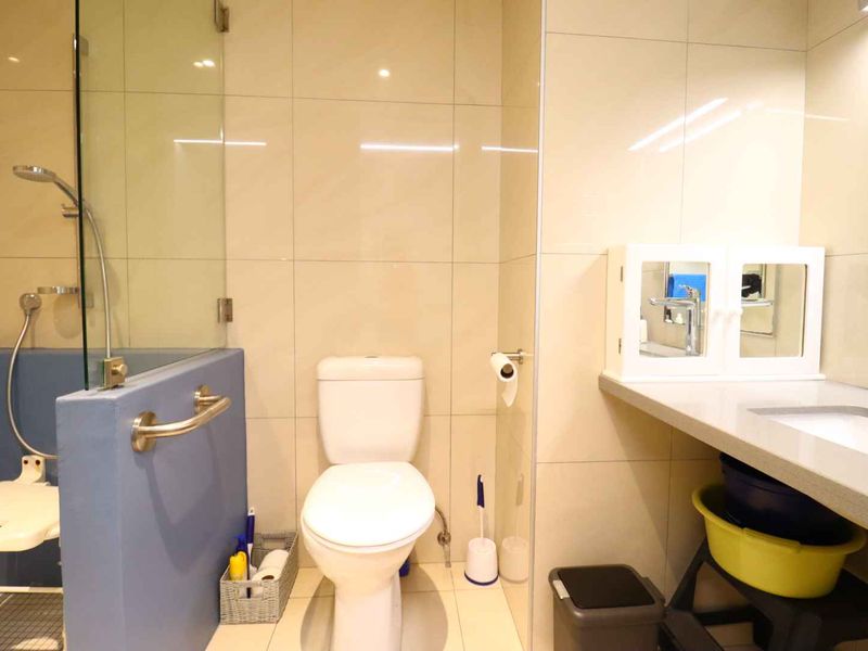 A functional bathroom featuring a glass-enclosed shower, a wall-mounted grab rail, a toilet, and a vanity countertop with an integrated sink.