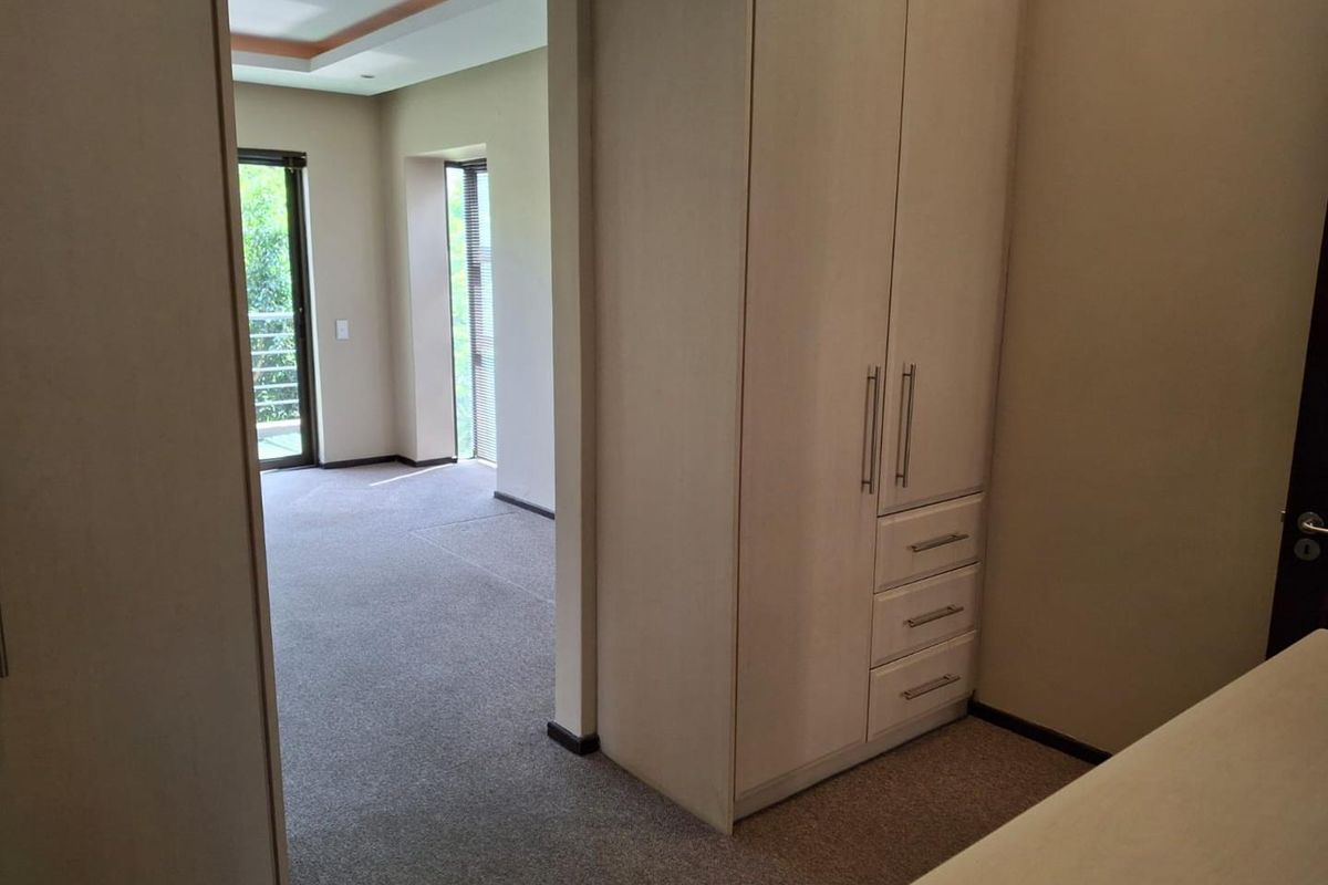 A spacious, empty bedroom featuring neutral carpeting, built-in cupboards, and access to a balcony through sliding glass doors.