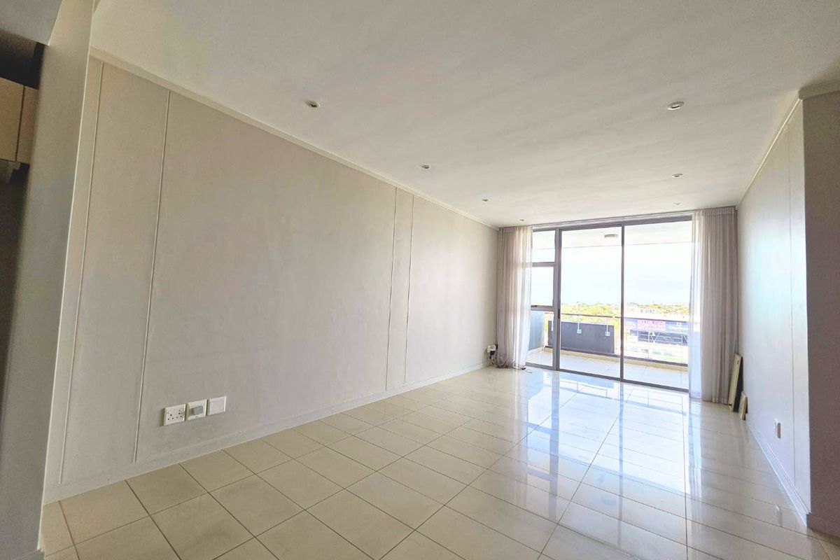 A bright, open-plan living area featuring neutral walls, polished tile flooring, recessed lighting, and direct access to a private balcony through sliding glass doors.