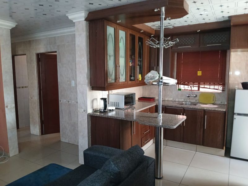 Open plan kitchen featuring dark wood cabinetry, granite countertops, a breakfast bar, and tiled flooring, seamlessly connecting to the adjacent living area.