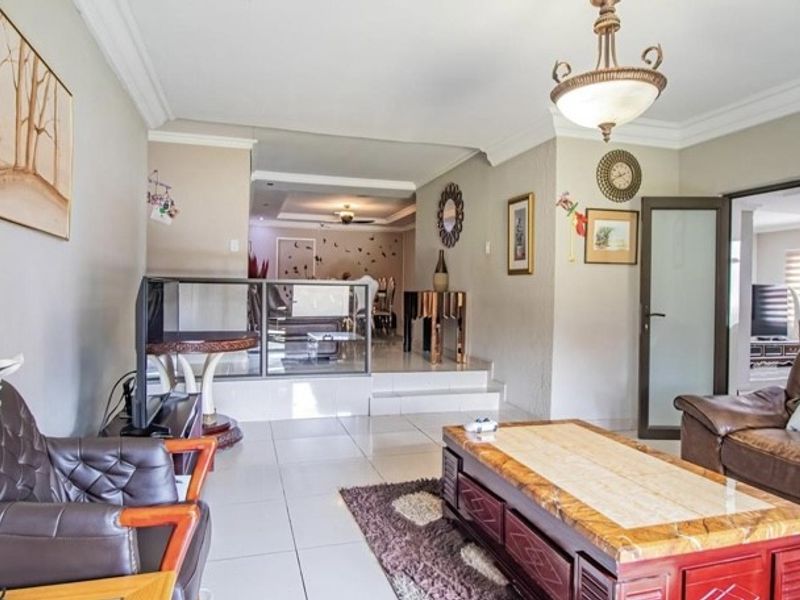 Spacious living area featuring tiled flooring, a raised platform with a glass balustrade, and coved ceiling details, creating a multi-level open-plan layout.