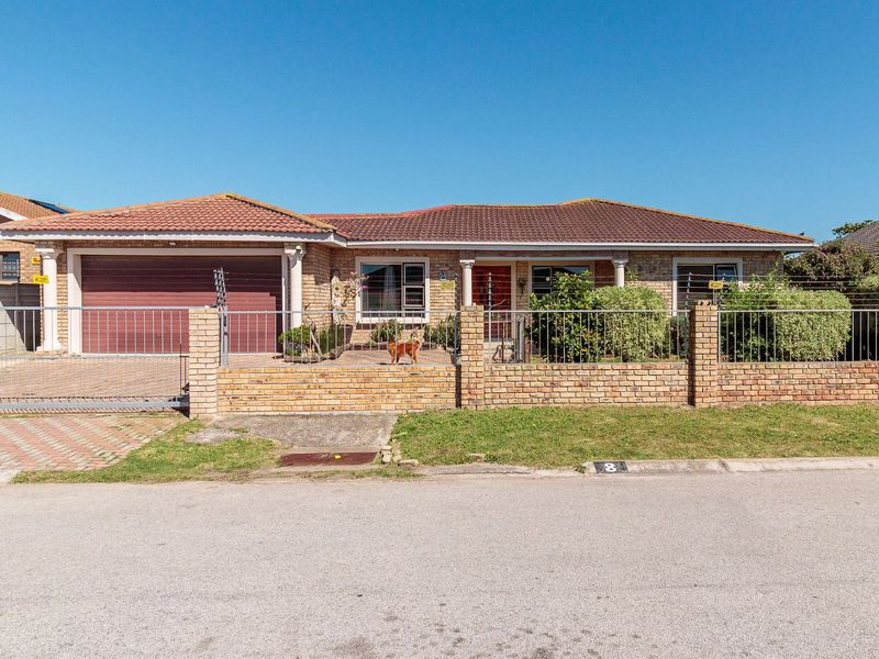 Front view of a single-story brick house featuring a tiled roof, a paved driveway, a garage, and a secure perimeter wall with a metal gate.