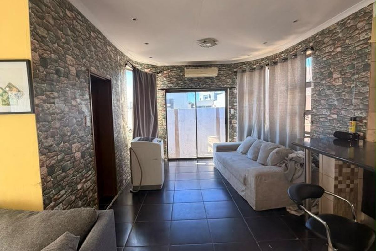 Open plan living area featuring stone-effect wallpaper, tiled flooring, recessed ceiling lighting, and sliding glass doors leading to an outdoor space.