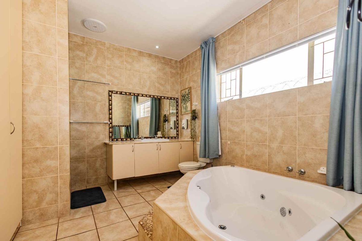 A spacious bathroom featuring a built-in corner jetted bathtub, tiled walls, and a vanity unit with a large wall-mounted mirror.