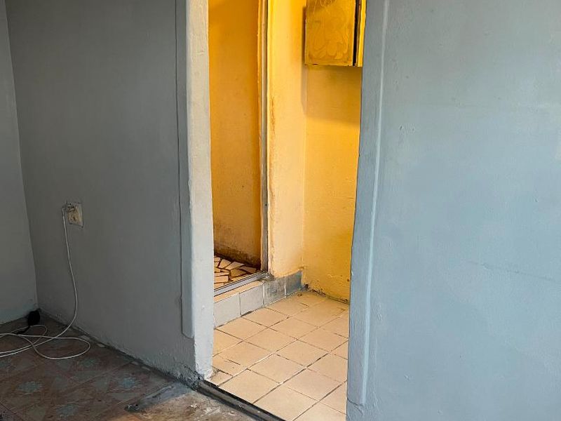 An empty bathroom space featuring an arched doorway, tiled flooring, and a shower enclosure, currently requiring renovation and finish updates.