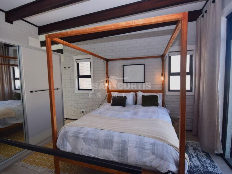 A well-maintained bedroom featuring exposed timber ceiling beams, painted brick walls, and a built-in sliding door wardrobe.