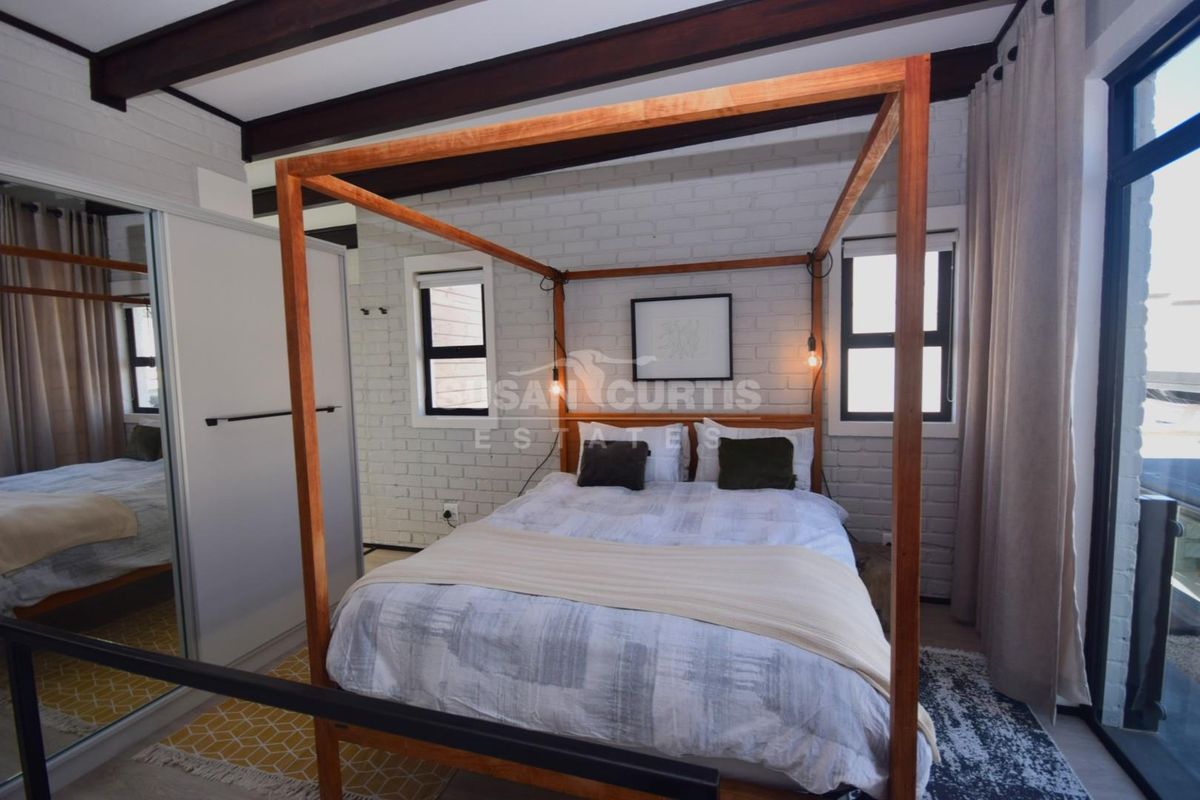 A well-maintained bedroom featuring exposed timber ceiling beams, painted brick walls, and a built-in sliding door wardrobe.