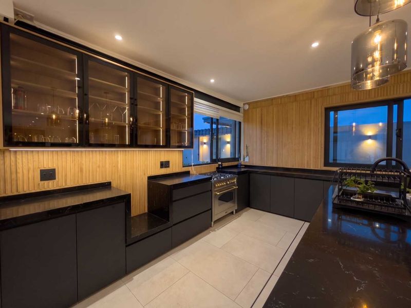 Modern kitchen featuring dark cabinetry, stone countertops, integrated lighting, and timber wall paneling, equipped with a built-in gas stove and oven.