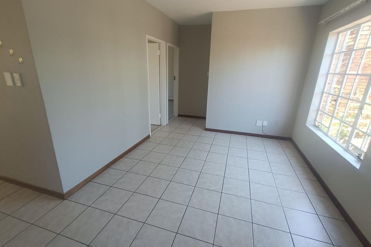 An empty, neutrally painted living area featuring tiled flooring and a large grid-pattern window, providing a clean and versatile space.