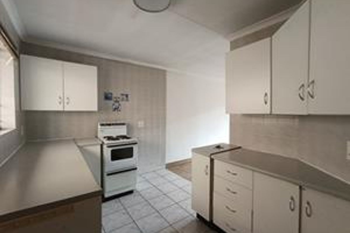 A functional kitchen featuring white cabinetry, laminate countertops, tiled flooring, and a freestanding stove, offering a clean and practical workspace.