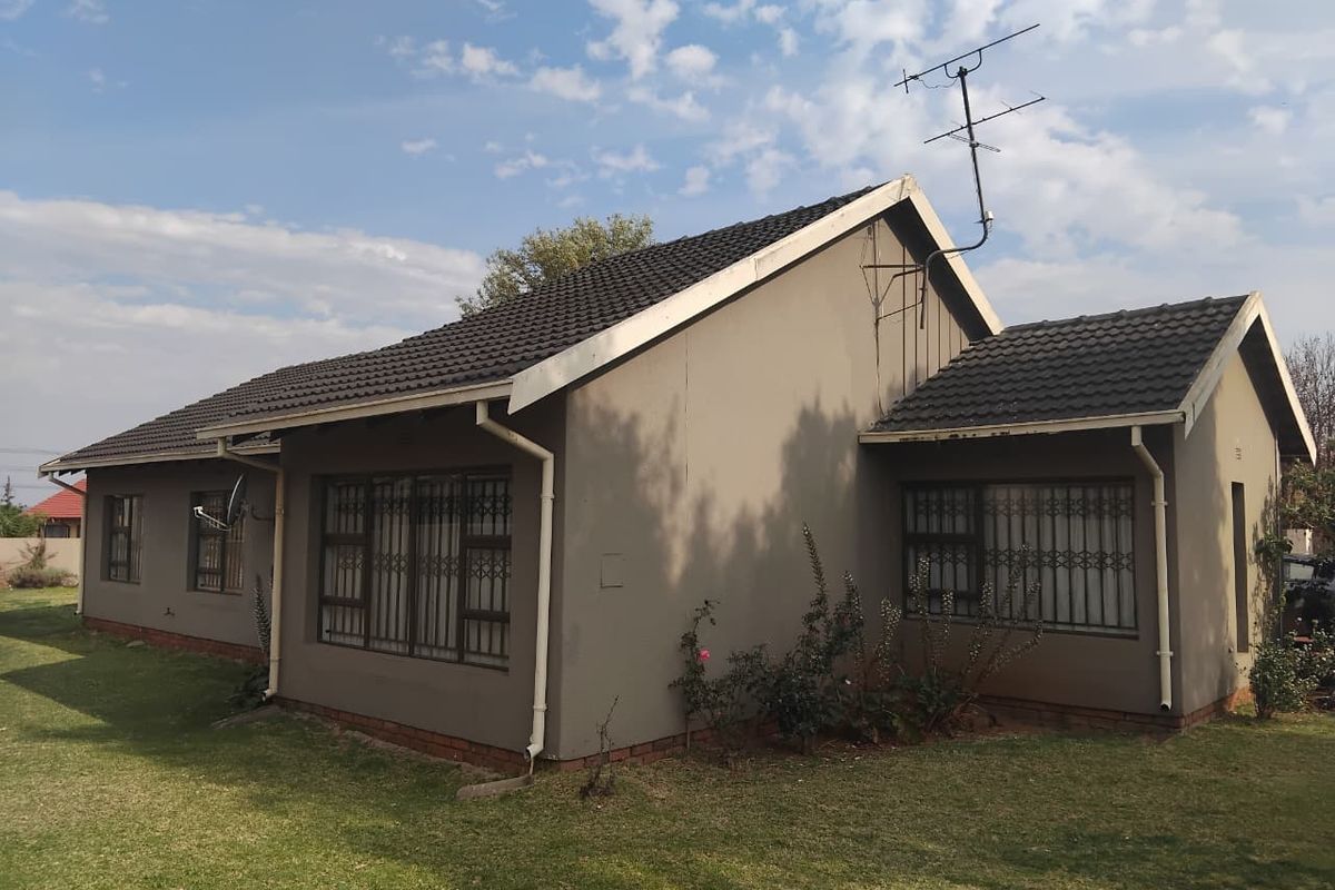 Rear view of a single-story residential house featuring a tiled roof, security bars on windows, and a surrounding lawn area.