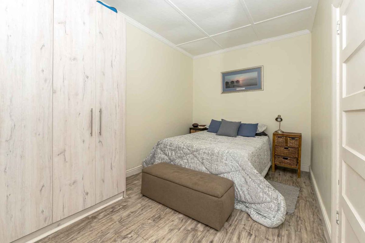 A compact bedroom featuring built-in wardrobes, wood-look laminate flooring, and a panelled ceiling.