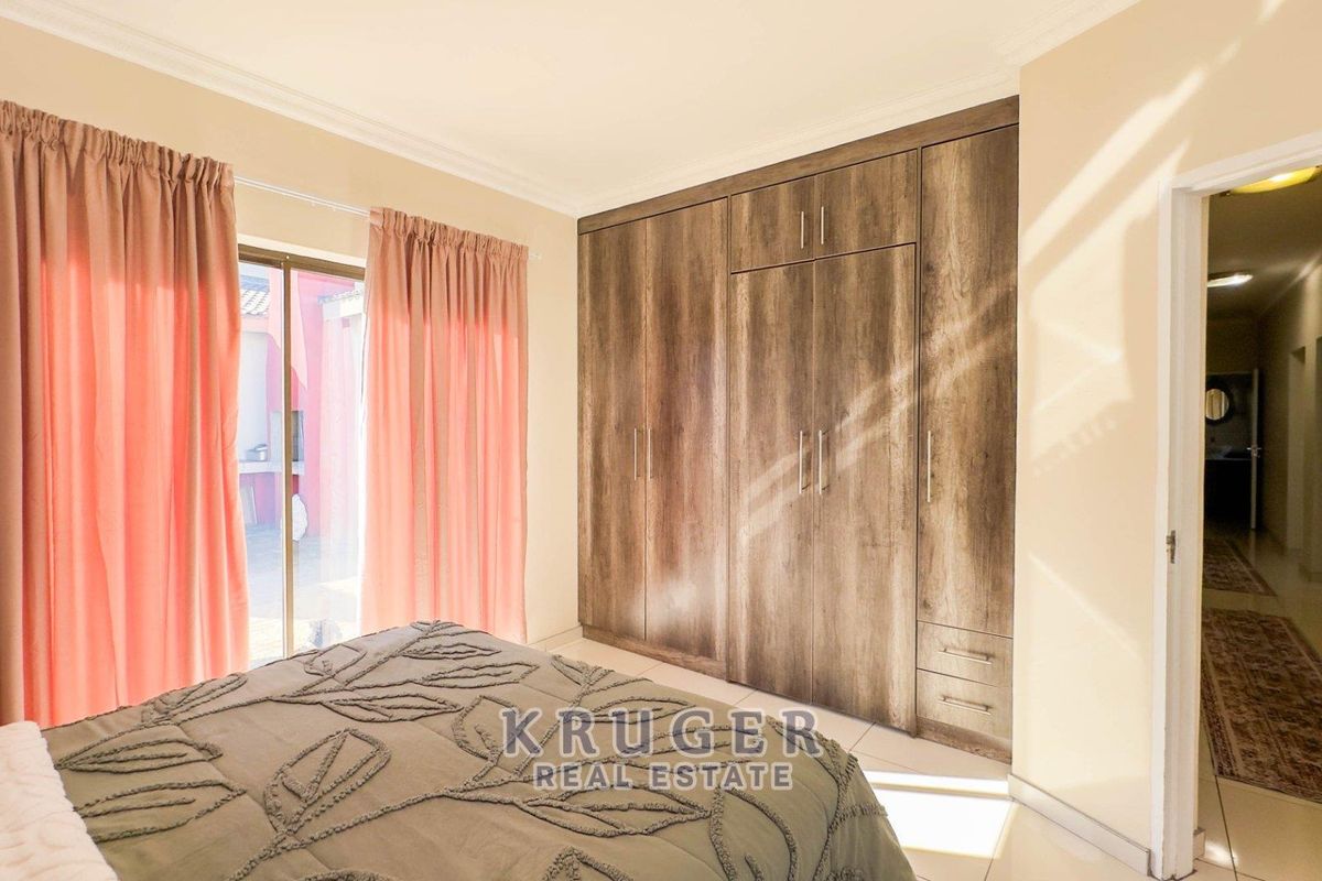 A well-lit bedroom featuring built-in wooden cupboards, tiled flooring, and sliding glass doors providing access to the exterior.