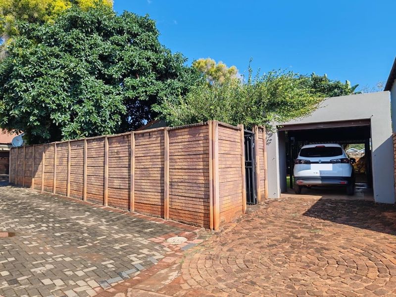 Front exterior view featuring a paved driveway, a covered carport, and a precast concrete boundary wall.