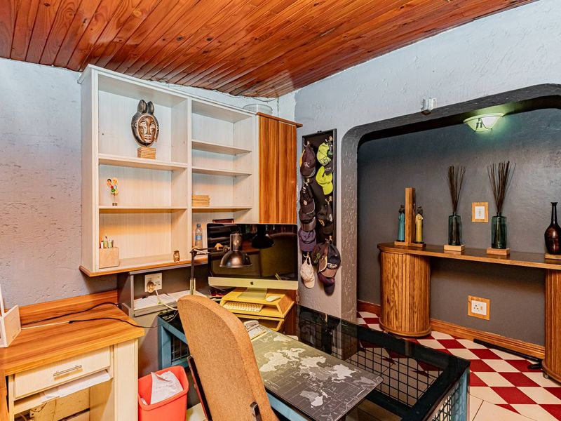 A home office space featuring built-in shelving, a timber-clad ceiling, and a secondary alcove area with a built-in console.