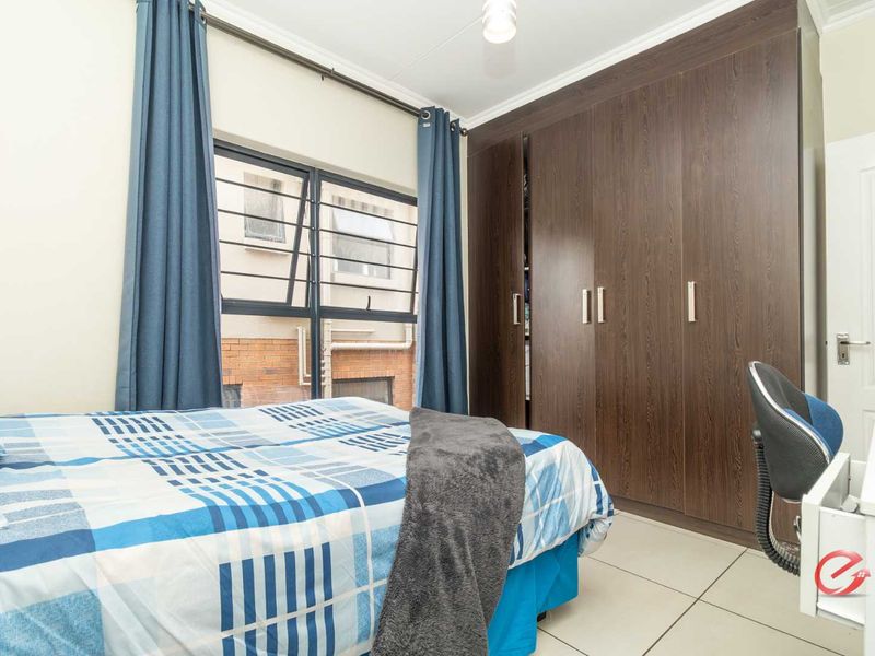 A bedroom featuring built-in dark wood-grain wardrobes, tiled flooring, and a window with security bars.