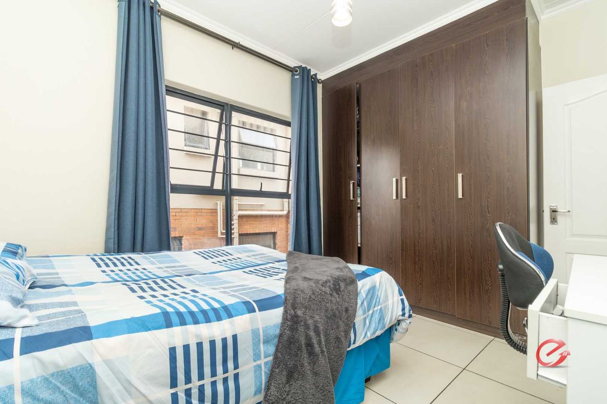 A bedroom featuring built-in dark wood-grain wardrobes, tiled flooring, and a window with security bars.