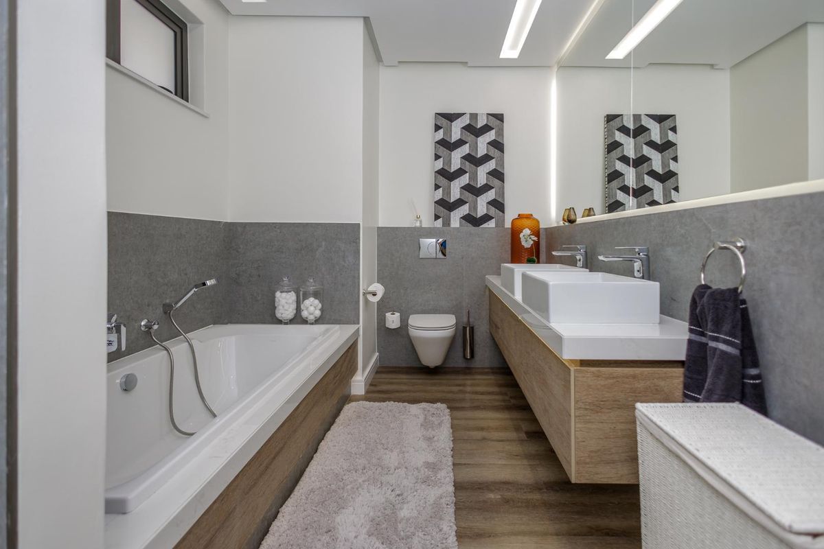 Modern bathroom featuring a double vanity with integrated sinks, wall-mounted toilet, and a built-in bathtub with contemporary grey tiling and wood-look flooring.