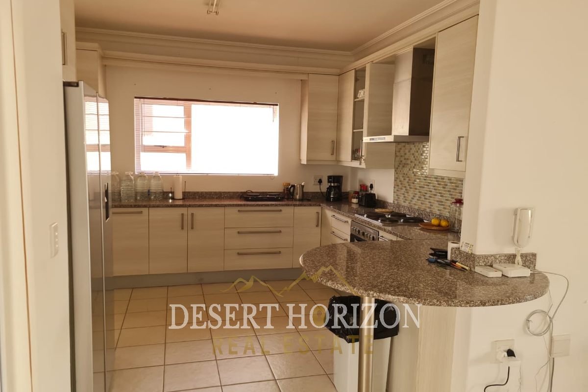 Functional kitchen featuring light-toned cabinetry, granite countertops, a breakfast bar, tiled flooring, and a mosaic tile backsplash.