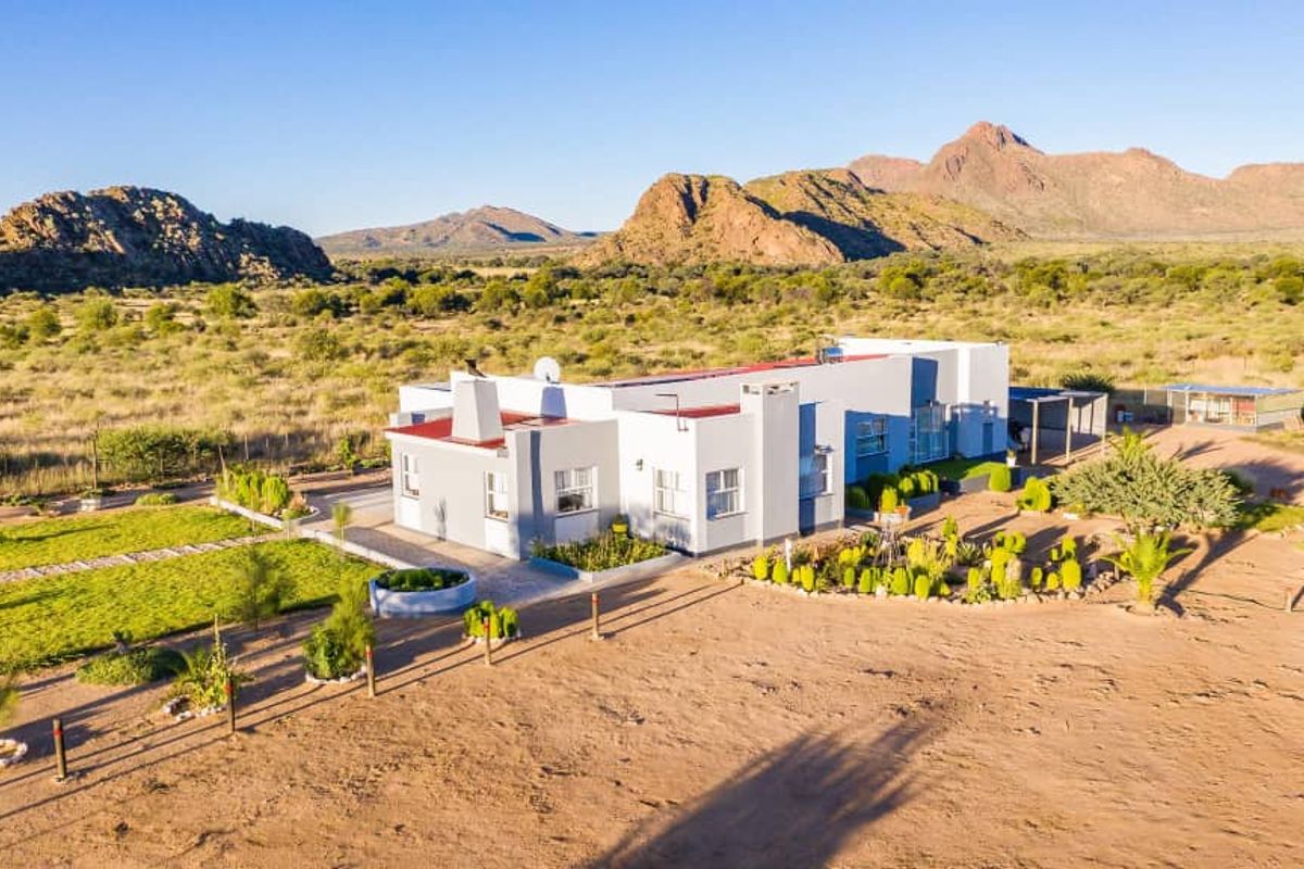 Aerial view of a single-story residential property set in a vast, arid landscape with mountain views, featuring a landscaped garden and paved areas.