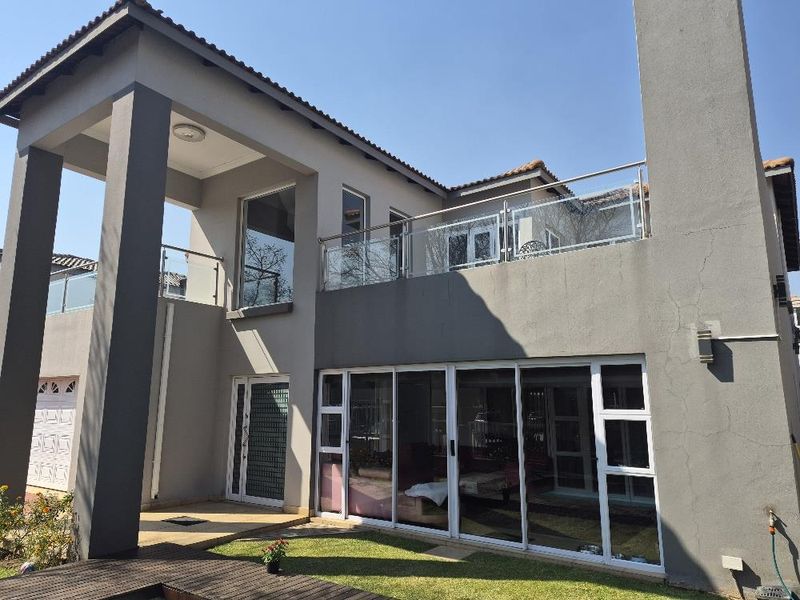 Rear elevation of a modern townhouse featuring a covered patio, upper-level balcony with glass balustrades, and large sliding glass doors.