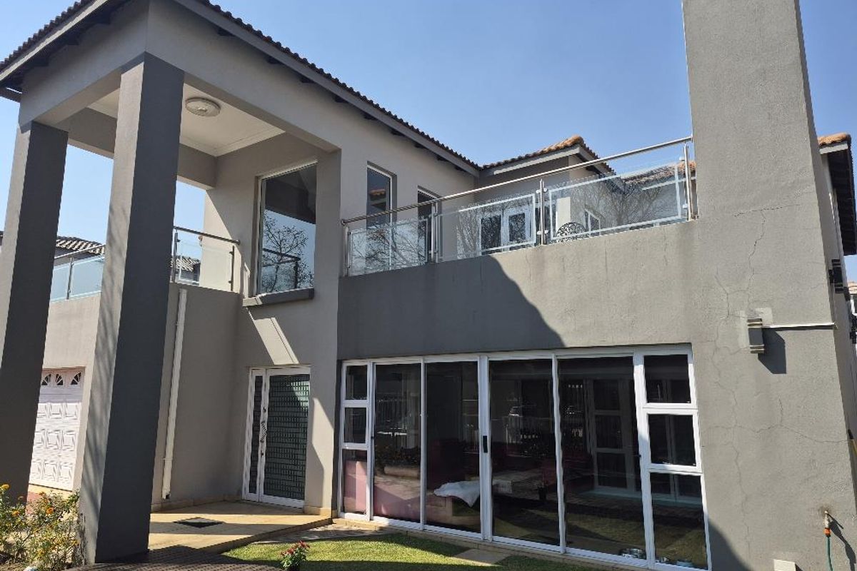 Rear elevation of a modern townhouse featuring a covered patio, upper-level balcony with glass balustrades, and large sliding glass doors.