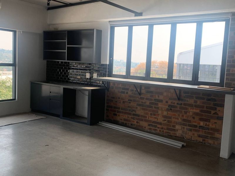 Modern industrial-style kitchen area featuring dark cabinetry, subway tile backsplash, exposed brickwork, and a built-in breakfast bar overlooking the exterior view.