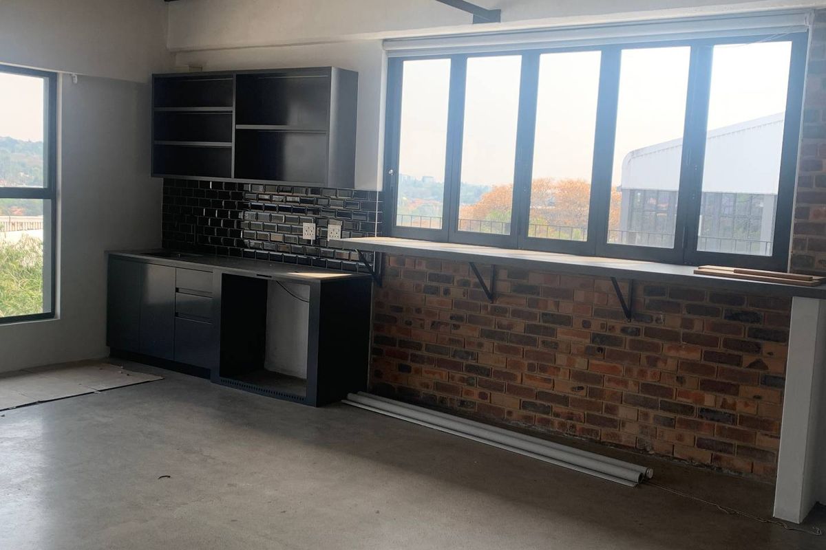 Modern industrial-style kitchen area featuring dark cabinetry, subway tile backsplash, exposed brickwork, and a built-in breakfast bar overlooking the exterior view.