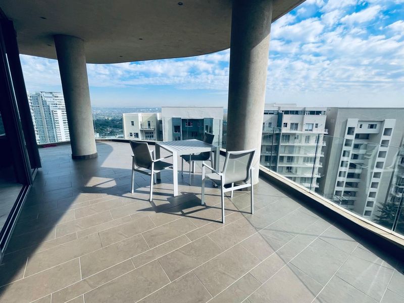 Spacious covered balcony featuring modern tiled flooring, glass balustrades, and expansive city views, providing an ideal outdoor living space.
