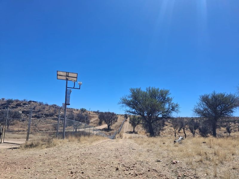 A view of the small holding property boundary featuring wire mesh fencing and a solar-powered security camera system.