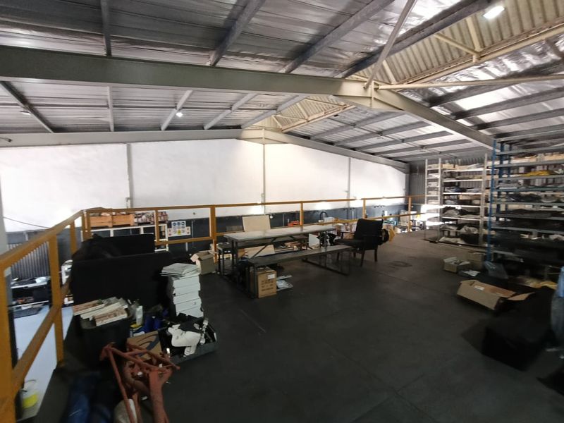 Industrial mezzanine level featuring exposed steel roof structure, safety railings, and integrated storage shelving, suitable for workshop or storage use.