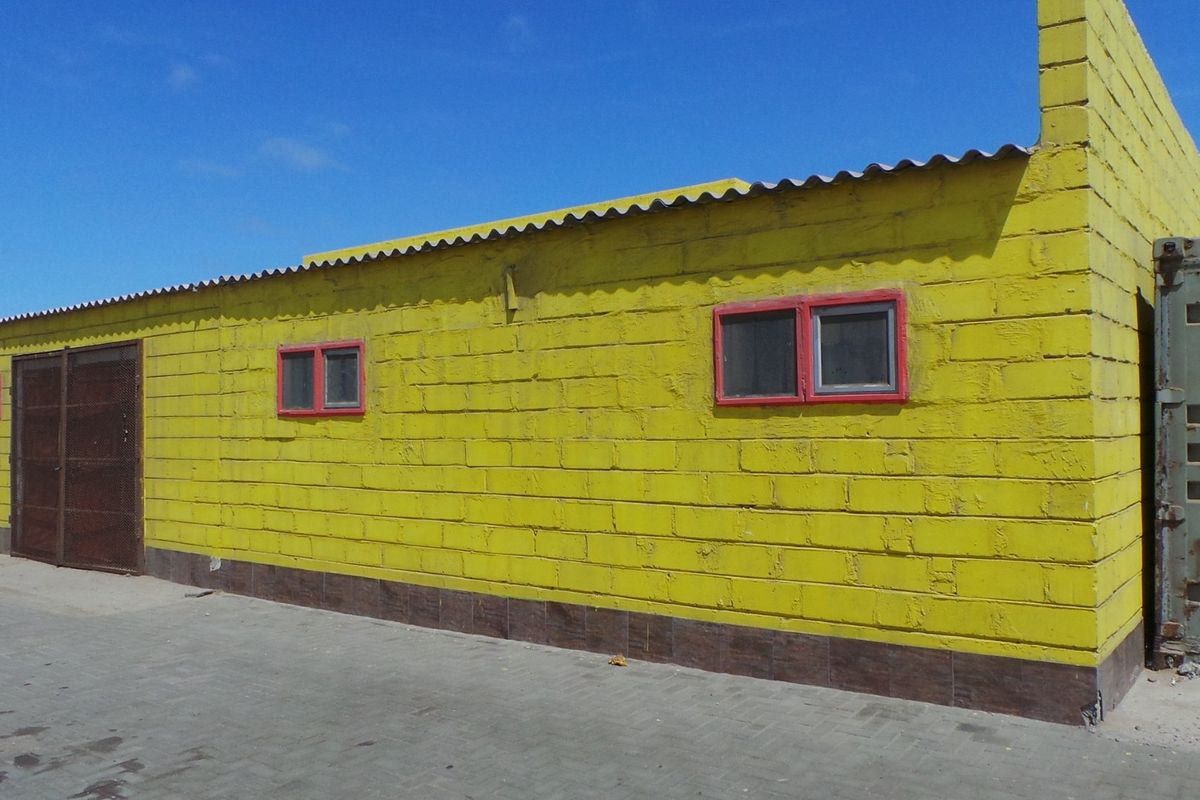 Exterior view of a yellow industrial building featuring block masonry construction, metal framed windows, and an attached shipping container storage unit.
