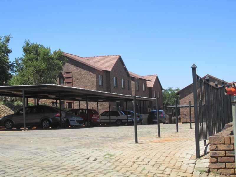 Exterior view of a brick apartment complex featuring a covered carport area and paved driveway with secure metal fencing.