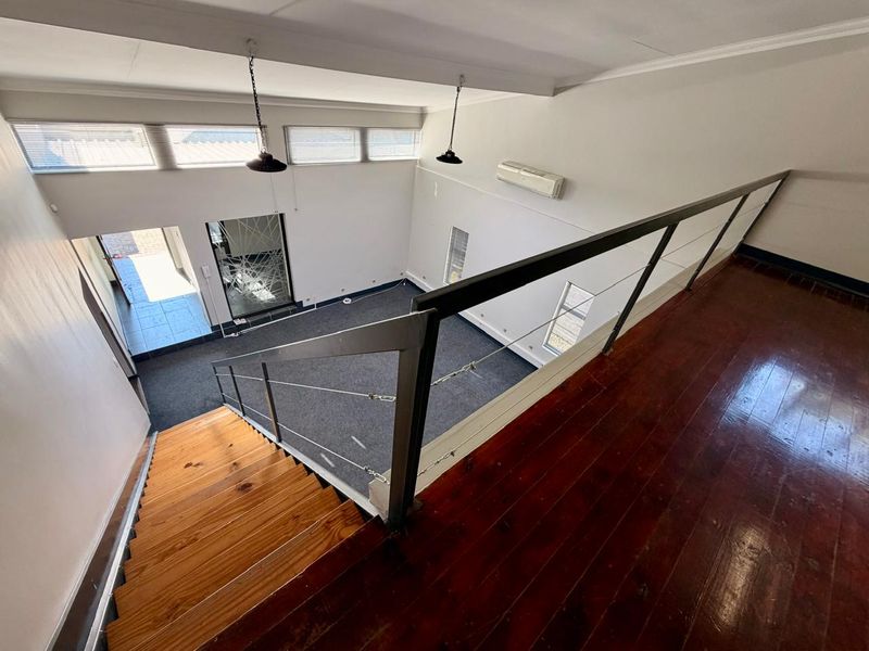 An elevated view looking down into a spacious living area featuring timber stairs, hardwood flooring, and high-level windows providing natural light.