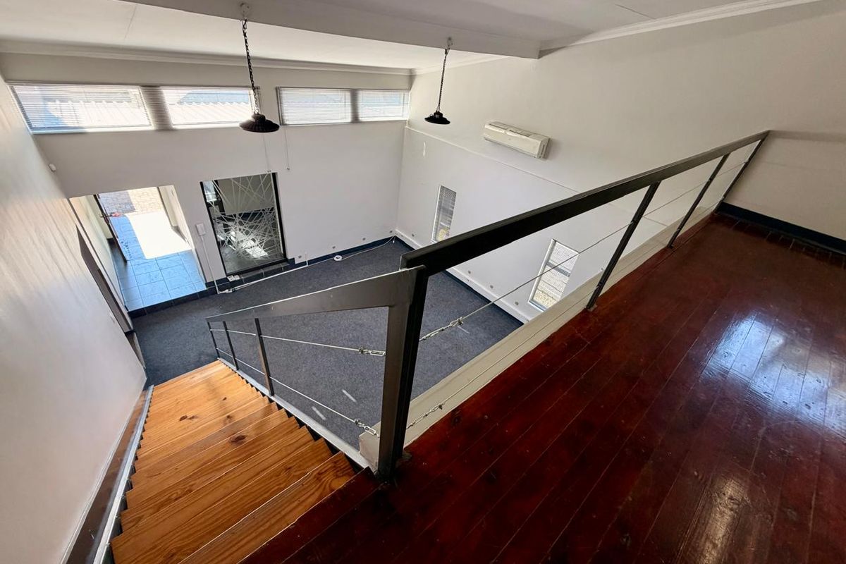 An elevated view looking down into a spacious living area featuring timber stairs, hardwood flooring, and high-level windows providing natural light.