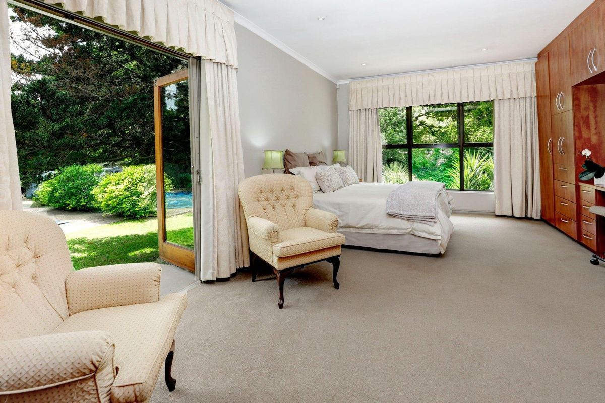 Spacious bedroom featuring built-in wooden cabinetry, neutral carpeting, and large glass doors opening directly to a lush garden and pool area.