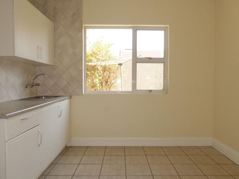 A clean, empty kitchen featuring white built-in cabinetry, tiled splashbacks, and neutral floor tiles, offering a functional space ready for personalization.
