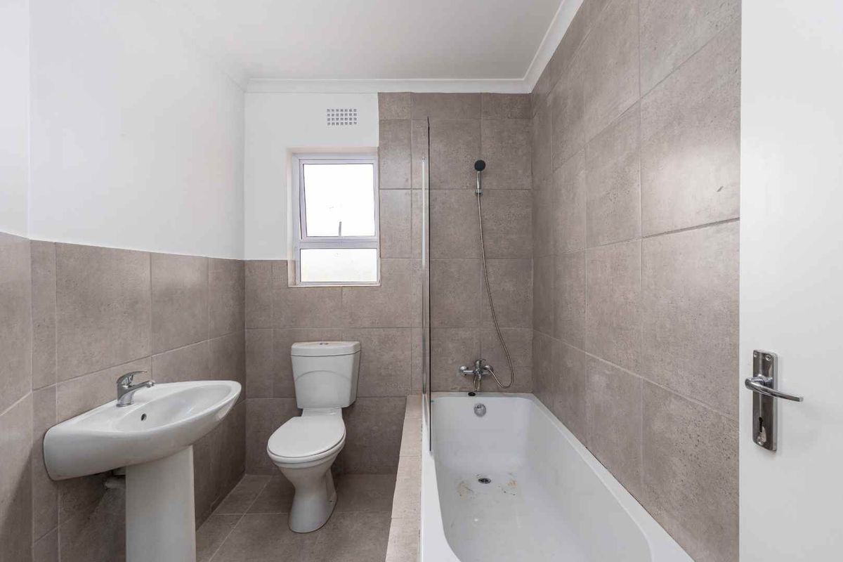 A functional bathroom featuring a pedestal basin, a standard toilet, and a bathtub with a glass shower screen and tiled wall finishes.