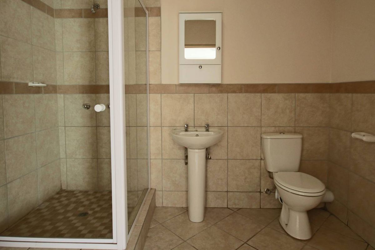 A functional bathroom featuring a glass-enclosed shower, pedestal basin, and toilet with neutral wall and floor tiling.