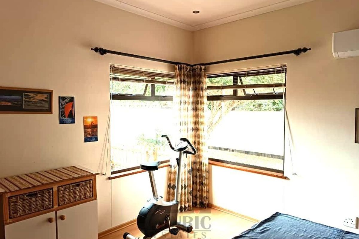 A bedroom featuring corner windows, laminate flooring, and a wall-mounted air conditioning unit.