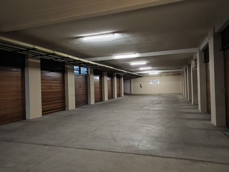 A spacious, well-lit underground parking garage featuring multiple individual garage units with wood-finish doors and concrete flooring.