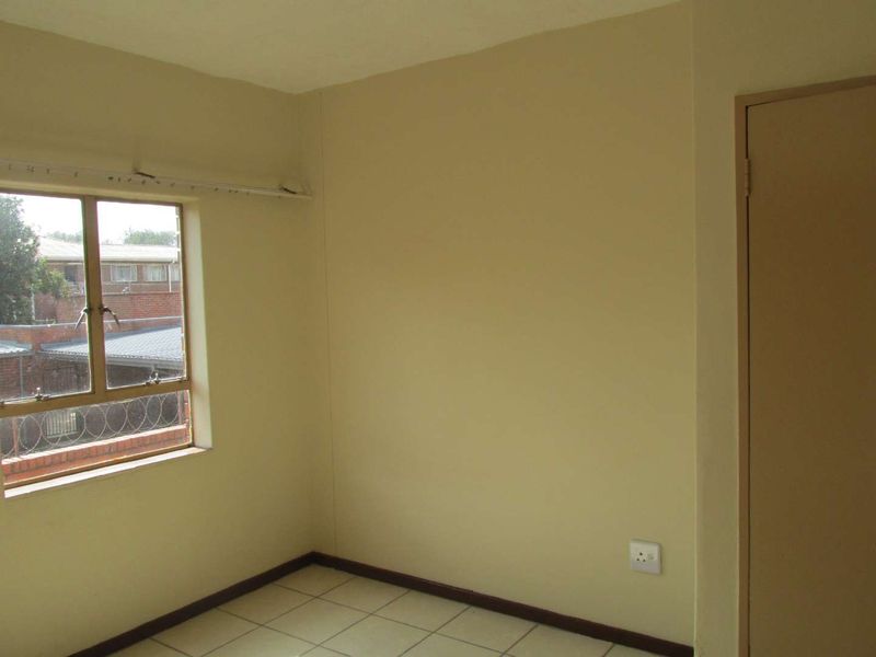 An empty bedroom featuring tiled flooring, a metal-framed window with security bars, and a neutral wall finish.
