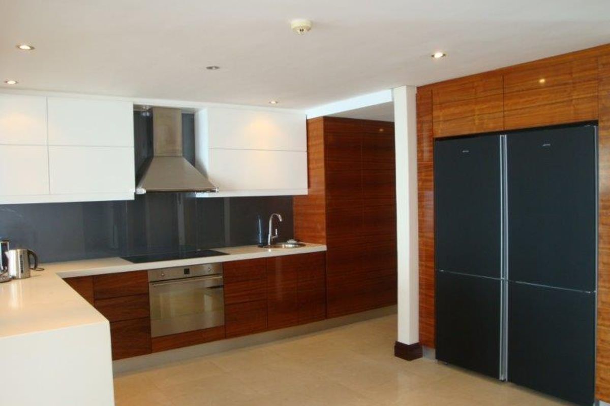 Modern kitchen featuring high-gloss wood cabinetry, white upper cabinets, integrated oven, stainless steel extractor fan, and sleek stone countertops.